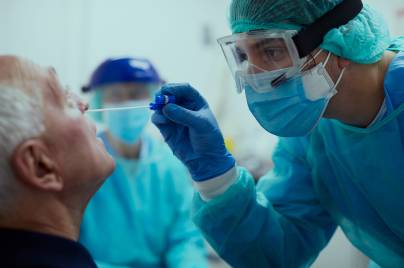 Ein Patient bekommt einen Nasenabstrich von einem Arzt mit Mundschutz und Schutzbrille.