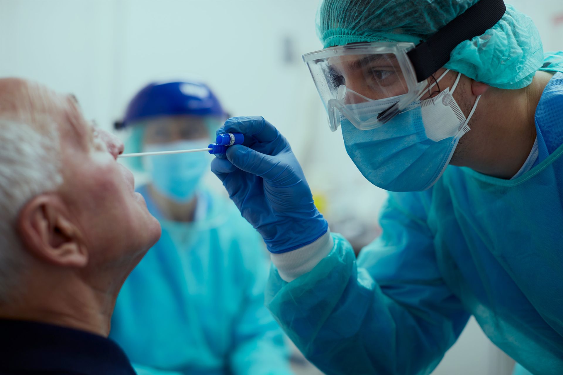 Ein Patient bekommt einen Nasenabstrich von einem Arzt mit Mundschutz und Schutzbrille.