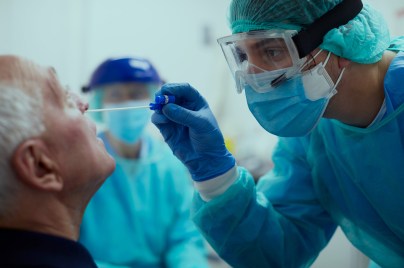 Ein Patient bekommt einen Nasenabstrich von einem Arzt mit Mundschutz und Schutzbrille.