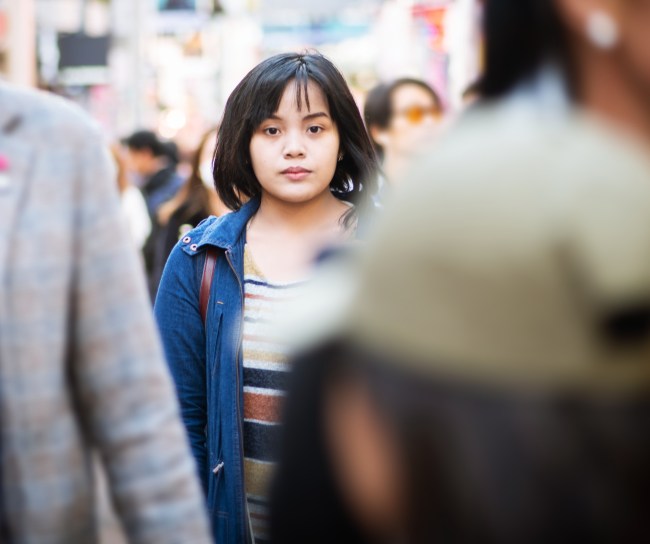 Eine junge Frau steht mitten auf einer belebten Straße und schaut in die Kamera.