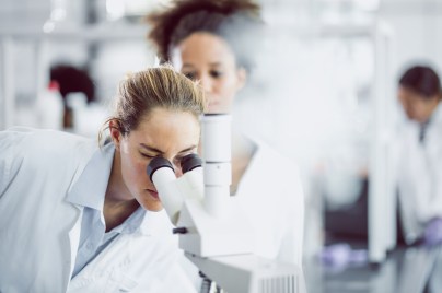 Eine Ärztin blickt im Labor durch ein Mikroskop.