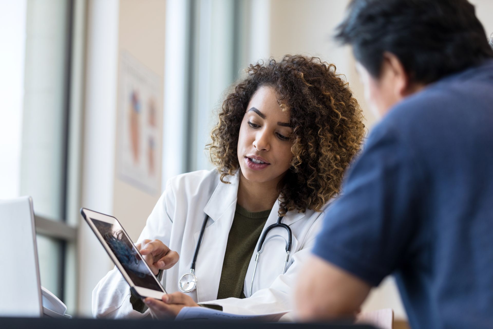 Eine Ärztin erklärt einem Patienten Details zu seiner Krankheit anhand eines Bildes auf ihrem Tablet.