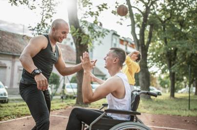 Zwei Männer klatschen beim Basketball-spielen ab. Einer von Ihnen sitzt im Rollstuhl