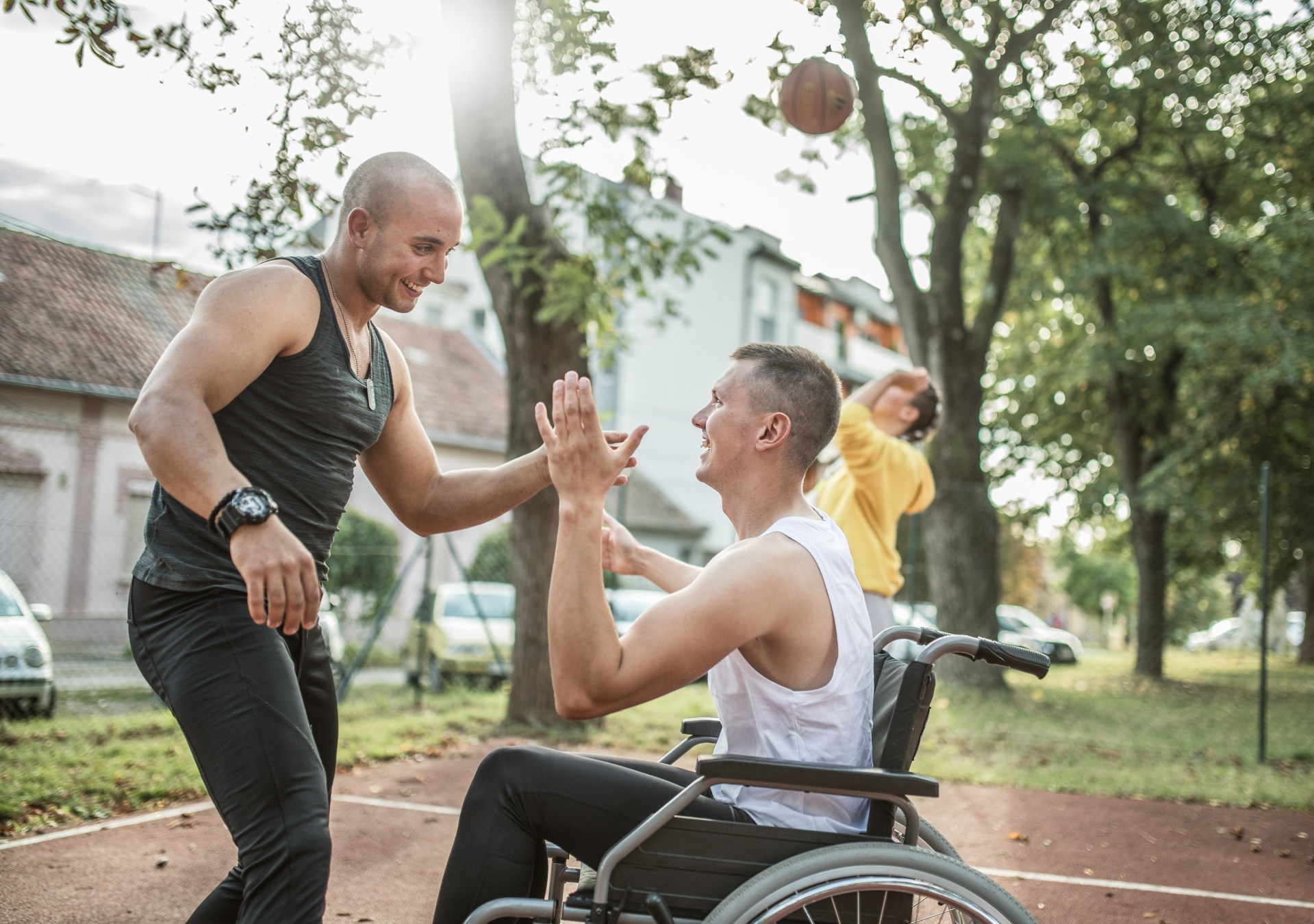 Zwei Männer klatschen beim Basketball-spielen ab. Einer von Ihnen sitzt im Rollstuhl