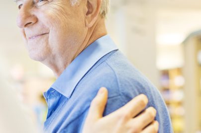 Ein Arzt berührt einen älteren Patienten fürsorglich an der Schulter und spricht ihm Mut zu.