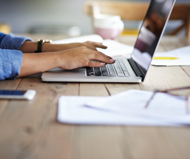 Eine Person sitzt am Schreibtisch und recherchiert mit einem Laptop.