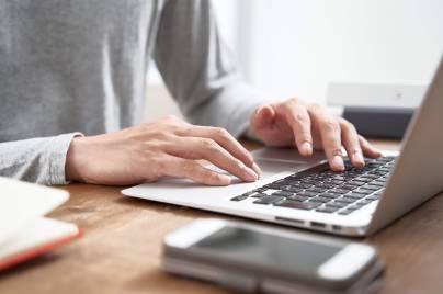 Eine Person sitzt am Schreibtisch und arbeitet am Laptop.