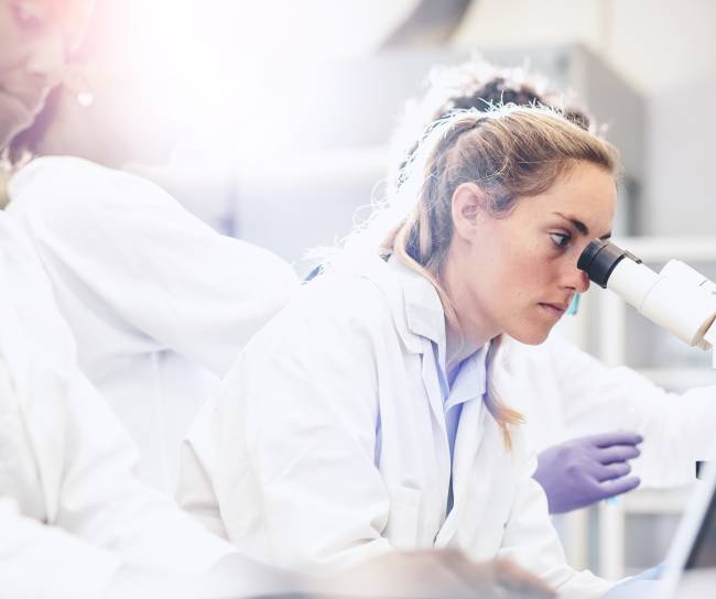 Eine Wissenschaftlerin sieht in ein Mikroskop.