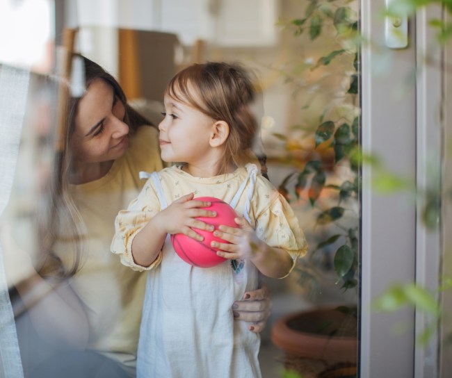 Mutter und Tochter stehen hinter einem Fenster und sehen sich glücklich an.