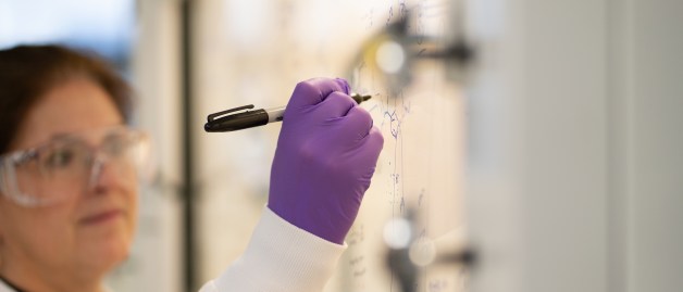 Eine Wissenschaftlerin macht sich auf der Glasscheibe einer sterilen Werkbank Notizen.