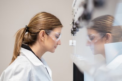 Eine Wissenschaftlerin steht vor einer sterilen Werkbank und sieht hinein.