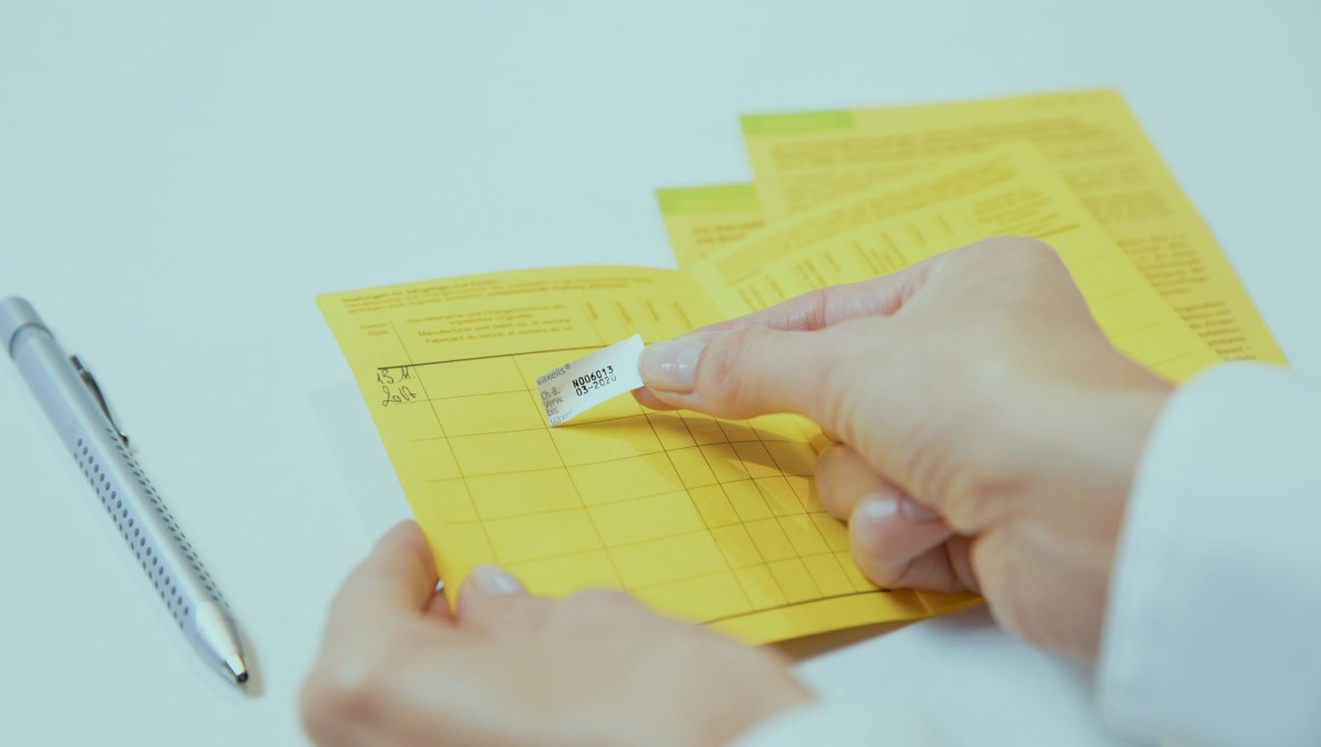 Impfsticker wird in einen Impfpass geklebt