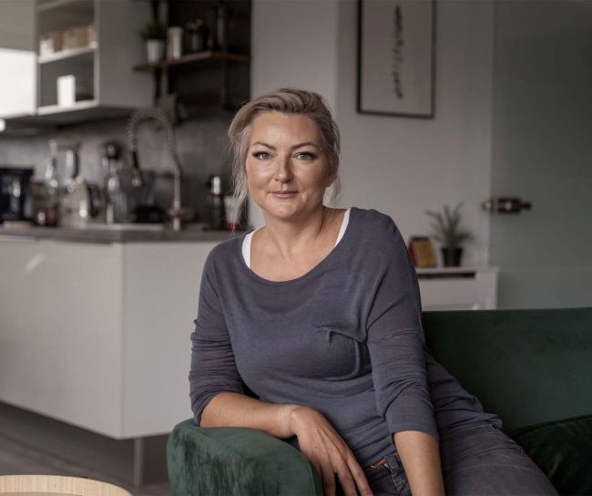 Moni sitzt auf einer grünen Couch bei ihr zuhause. In wohnlicher Atmosphäre und mit entspanntem Look posiert sie für ein Foto.