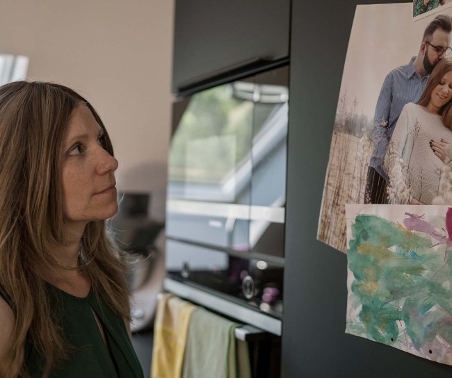 Silja steht vor ihrem Kühlschrank. Sie betrachtet ein Foto, das mit einem Magneten befestigt ist. Es zeigt sie als Schwangere gemeinsam mit ihrem Mann.