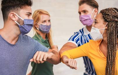 Vier Personen mit Masken die ihre Ellenbogen sternförmig zusammendrücken