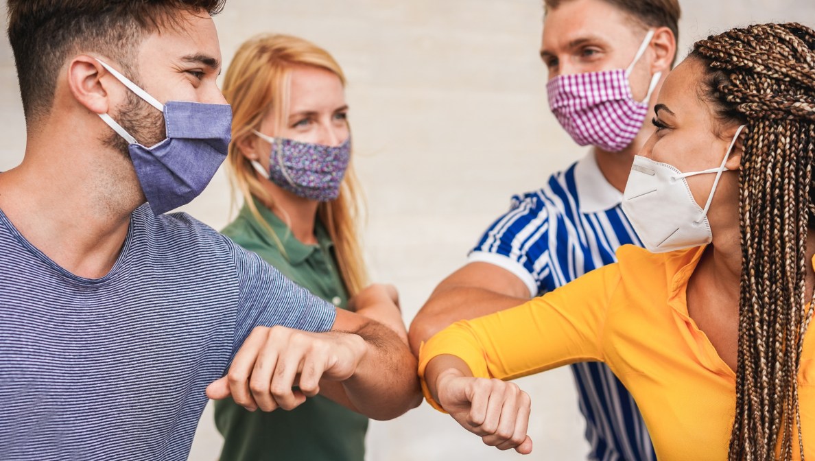 Vier Personen mit Masken die ihre Ellenbogen sternförmig zusammendrücken