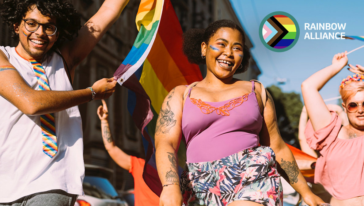 Das Bild zeigt tanzende Menschen bei einer Parade. Im Vordergrund schwingt ein Mann eine Regenbogenfahne und trägt eine Regenbogenkrawatte. Eine Frau hat Regenbogen auf die Wangen gemalt. In der oberen rechten Ecke des Bildes ist das Logo der MSD Rainbow Alliance eingefügt.