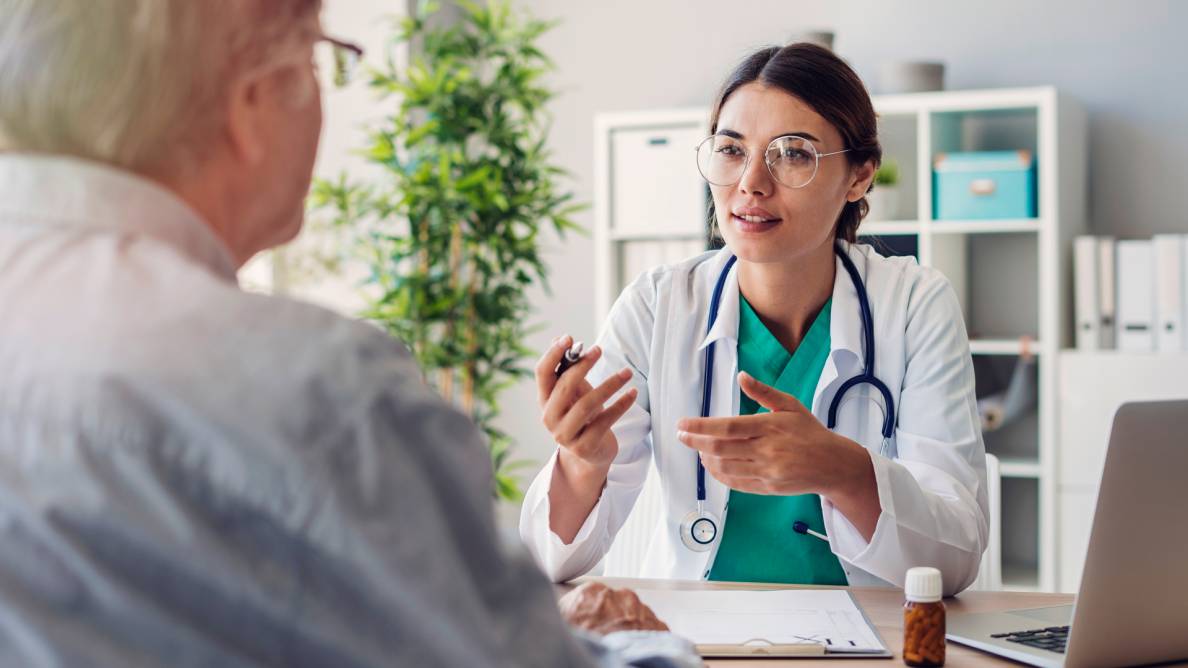 Eine junge Ärztin erklärt einem Patienten etwas. Die Ärztin ist mit dem Gesicht der Kamera zugewandt. Den Patienten sieht man lediglich seitlich von hinten, sodass nur ein Teil des Rückens und des Gesichts zu sehen ist.