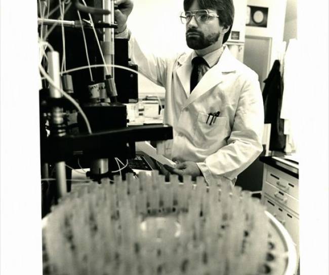 Historisches schwarz-weiß Bilds eines Forschers bei MSD, der eine Maschine in einem Labor betätigt.