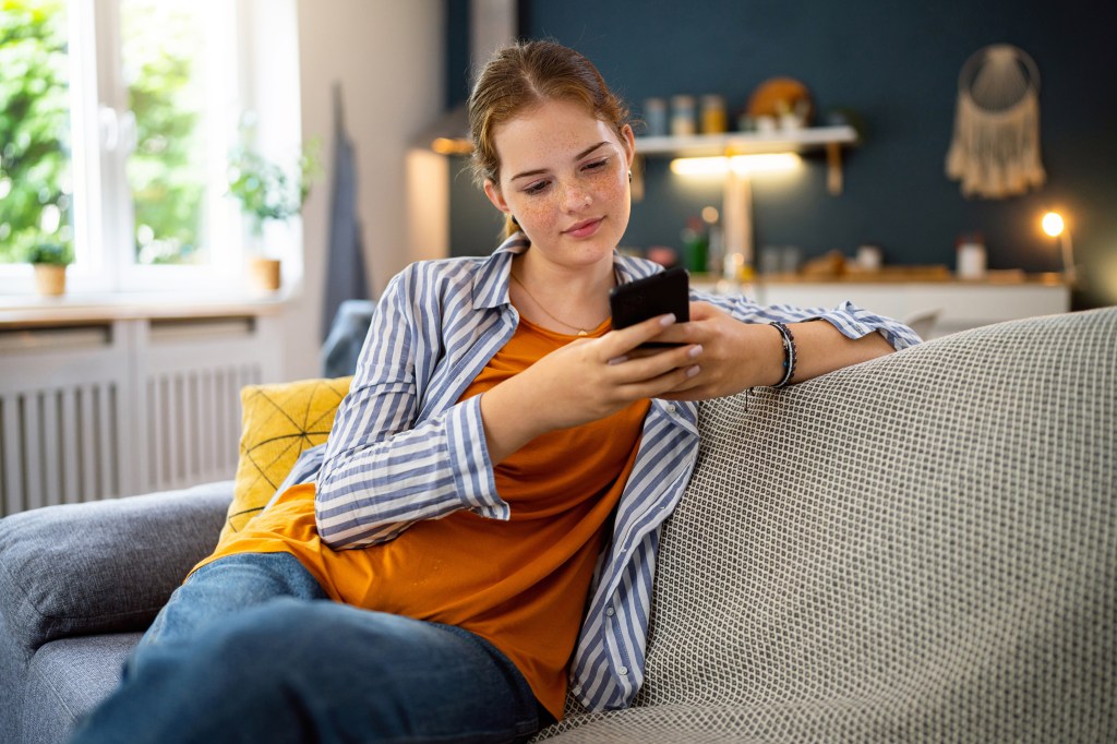 Mädchen sitzt mit ihrem Smartphone auf dem Sofa.